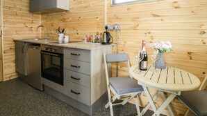 Eine kleine Küche mit Spüle, Herd und Schränken, ein Esszimmertisch mit Stühlen und ein Fenster für natürliches Licht.