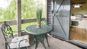 Ein überdachter Außenbereich mit Tisch und Stühlen, einer Tür und Blick auf Bäume.