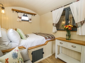 Quarto aconchegante com cama, mesa de cabeceira, janela com cortinas e um vaso com flores.