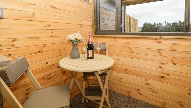 A small wooden room with a table and chairs, a window, and a bottle of wine. - Thornhills Lodge (Bridgwater)