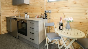 A compact kitchen with a sink, stove, and cabinets, a small dining table with chairs, and a window providing natural light. - Thornhills Lodge (Bridgwater)