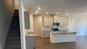 A modern kitchen with a central island, built-in appliances, and a staircase leading to another level.