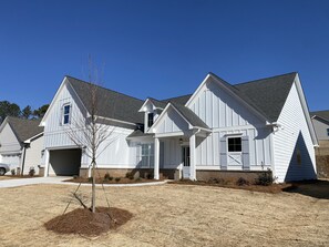 Stylish single-story home with a central entrance and two windows on each side, set amidst a charming front yard with a small tree.