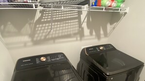 A laundry area with two black washing machines and a shelf above containing cleaning supplies.