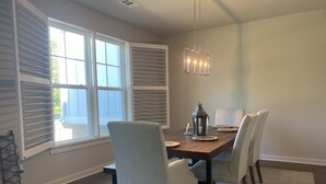 A dining area with a wooden table, four chairs, a chandelier, and a window with blinds.