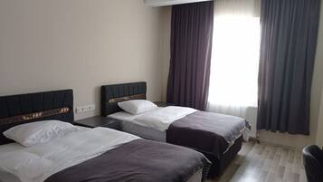A hotel room with two beds, a wooden headboard, a window with curtains, and a radiator.