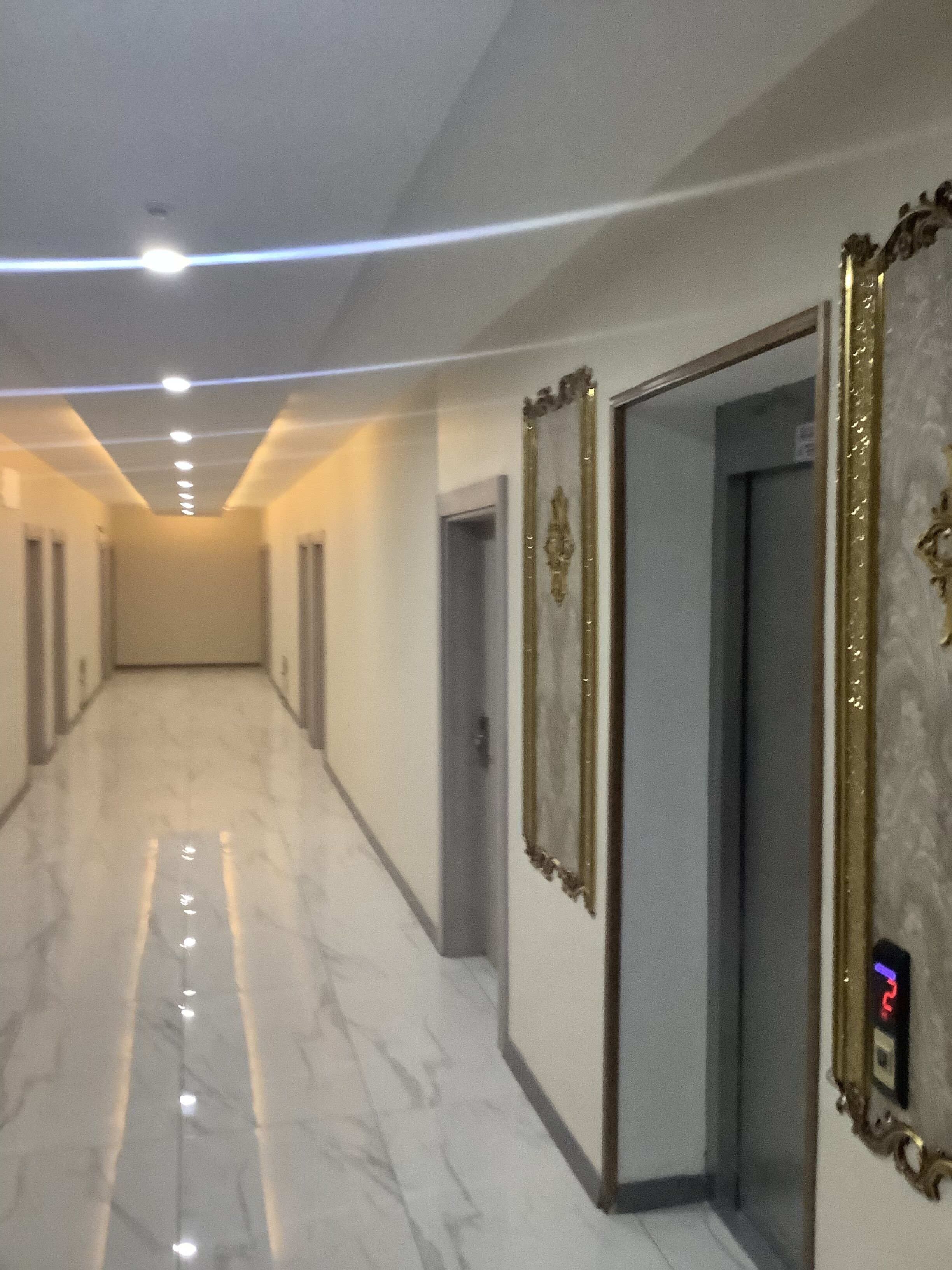 Un pasillo con suelo de mármol, una puerta con espejo y una pantalla digital en la pared.