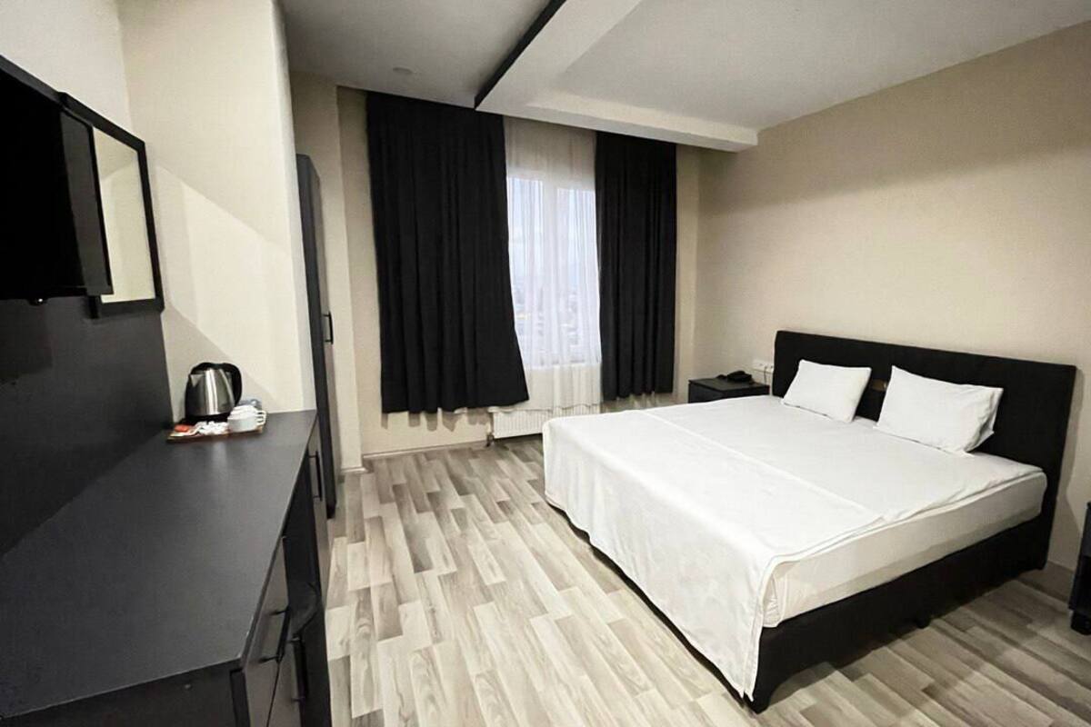 A hotel room with a bed, bedside table, and a desk with a kettle.