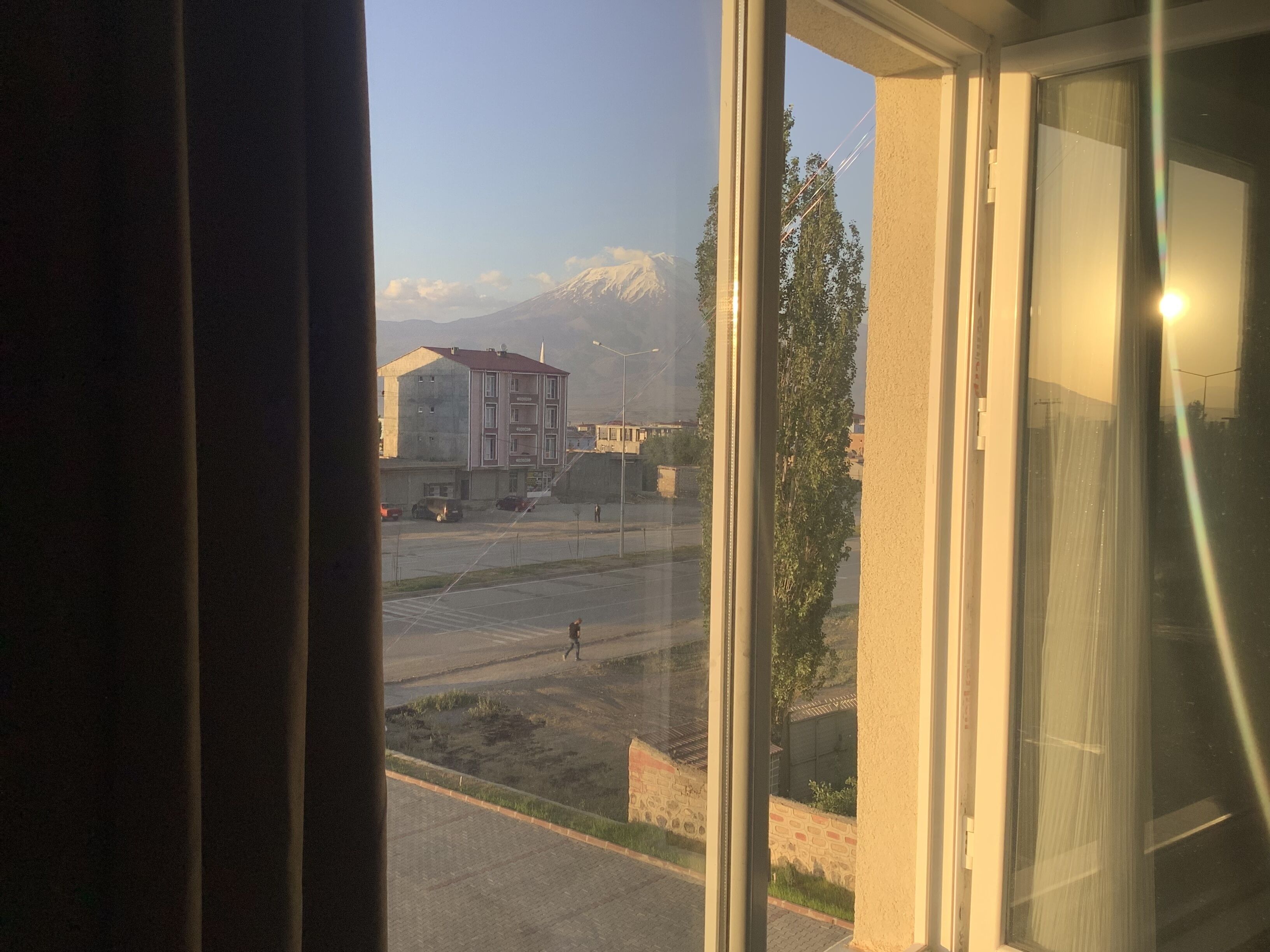 A view from inside a building, looking out through a window. There is a street with a few cars and a building with a red roof.