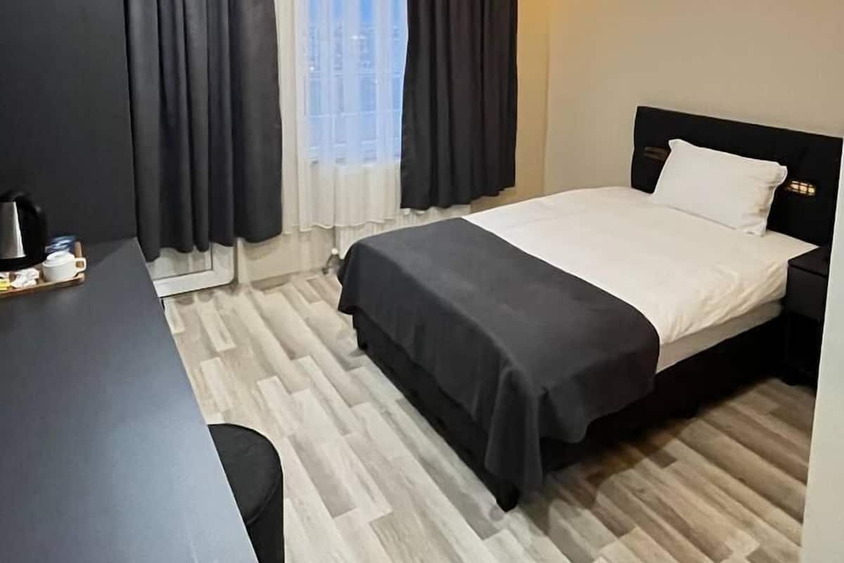 A modern hotel room with a bed, a desk, and a large window with curtains.