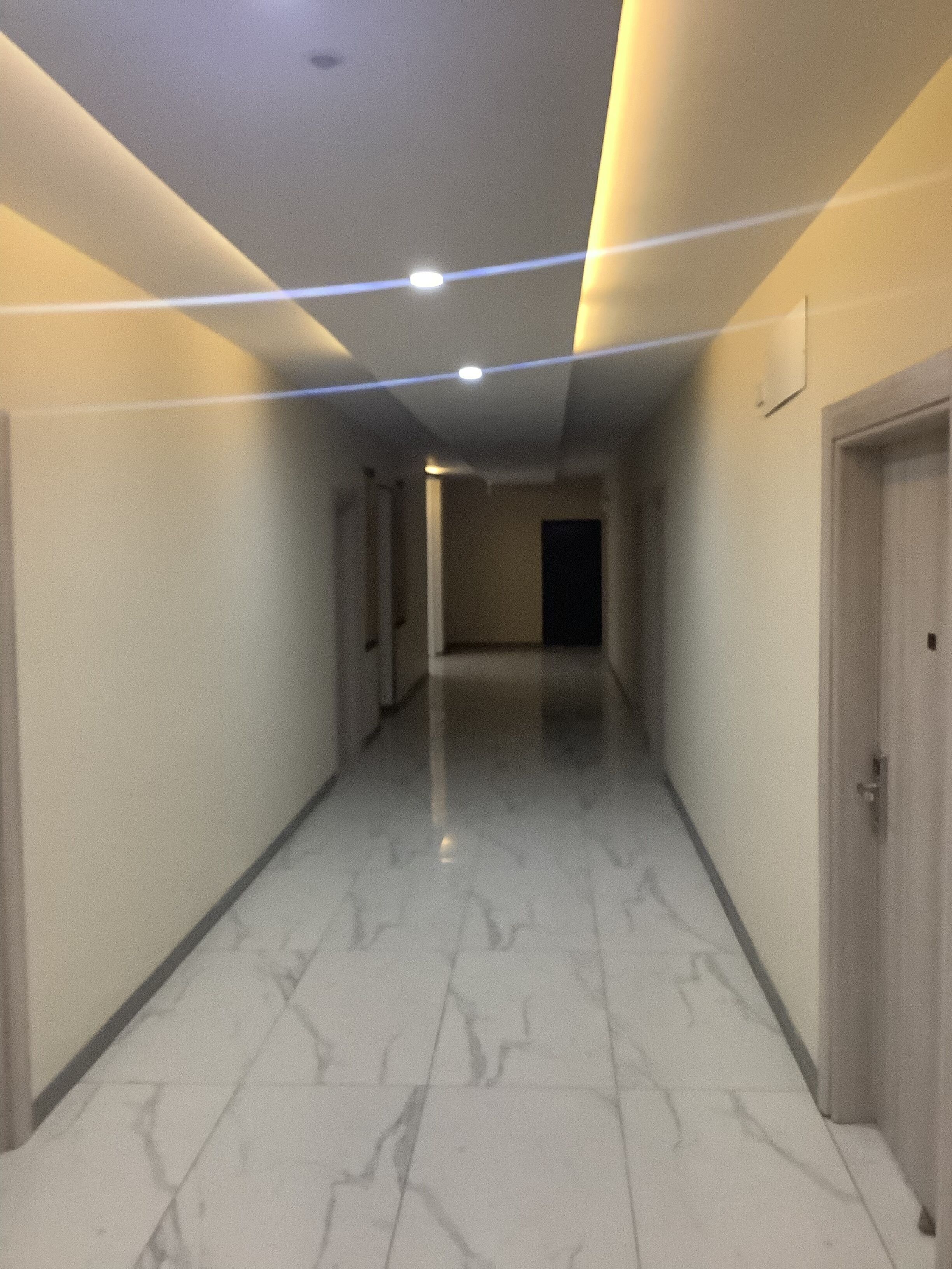 Un pasillo con suelo de mármol, puertas a ambos lados e iluminación empotrada en el techo.