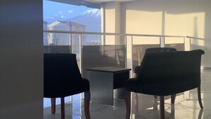 A modern interior with a glass partition, two chairs, a small table, and a view of a mountain. - Atlihan Plus Hotel (Dogubayazit)