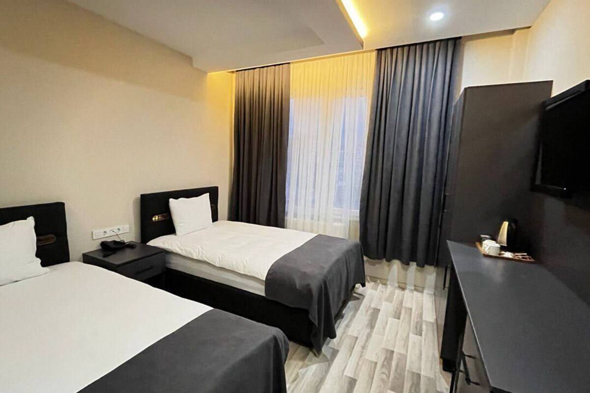 A hotel room with two beds, a desk, a TV, and a window with curtains.