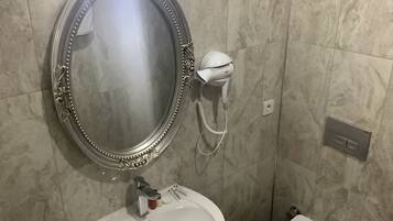 A bathroom with a marble wall, a round mirror with a decorative frame, a white sink, and a toilet.