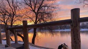 Un pontile di legno che si affaccia su un lago ghiacciato con un tramonto sullo sfondo.
