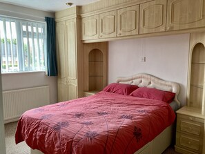 Une chambre à coucher avec un lit, une fenêtre avec des rideaux et des armoires en bois.
