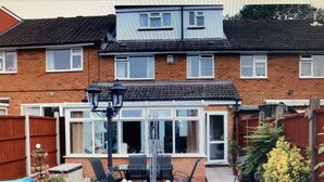 A two-story brick house with a conservatory, a patio with outdoor furniture, and a garden area with potted plants. - Quiet rooms in a terraced house easy walking to shops, train (Birmingham)