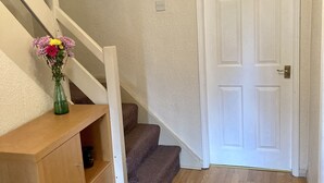 A staircase leading to a door, a wooden console table with a vase of flowers, and a framed picture on the wall. - Quiet rooms in a terraced house easy walking to shops, train (Birmingham)