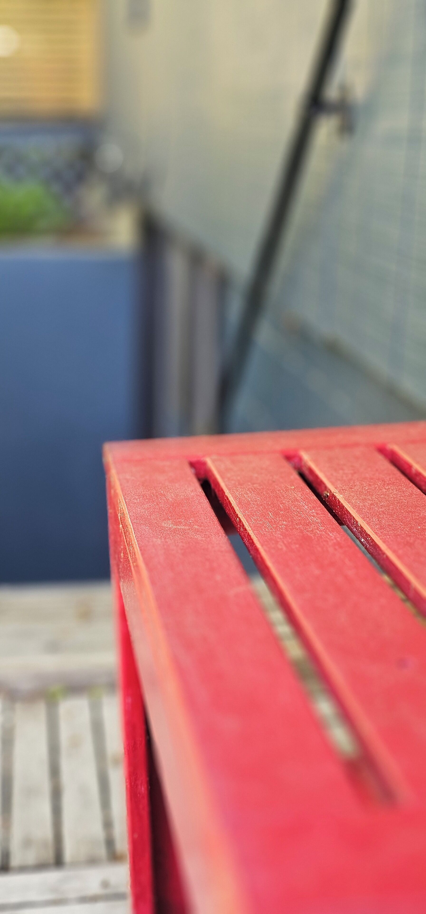 A close-up of a red bench with a metal frame, set against a blurred background.