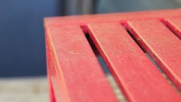 A close-up of a red bench with a metal frame, set against a blurred background.