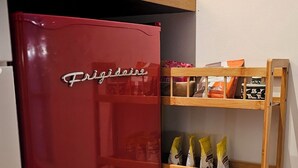 A compact kitchen with a red Frigidaire refrigerator, wooden shelves with food items, and a microwave on top. - Hibiscus Suite - Private Studio Apartment in Rhinebeck Village (RHINEBECK)