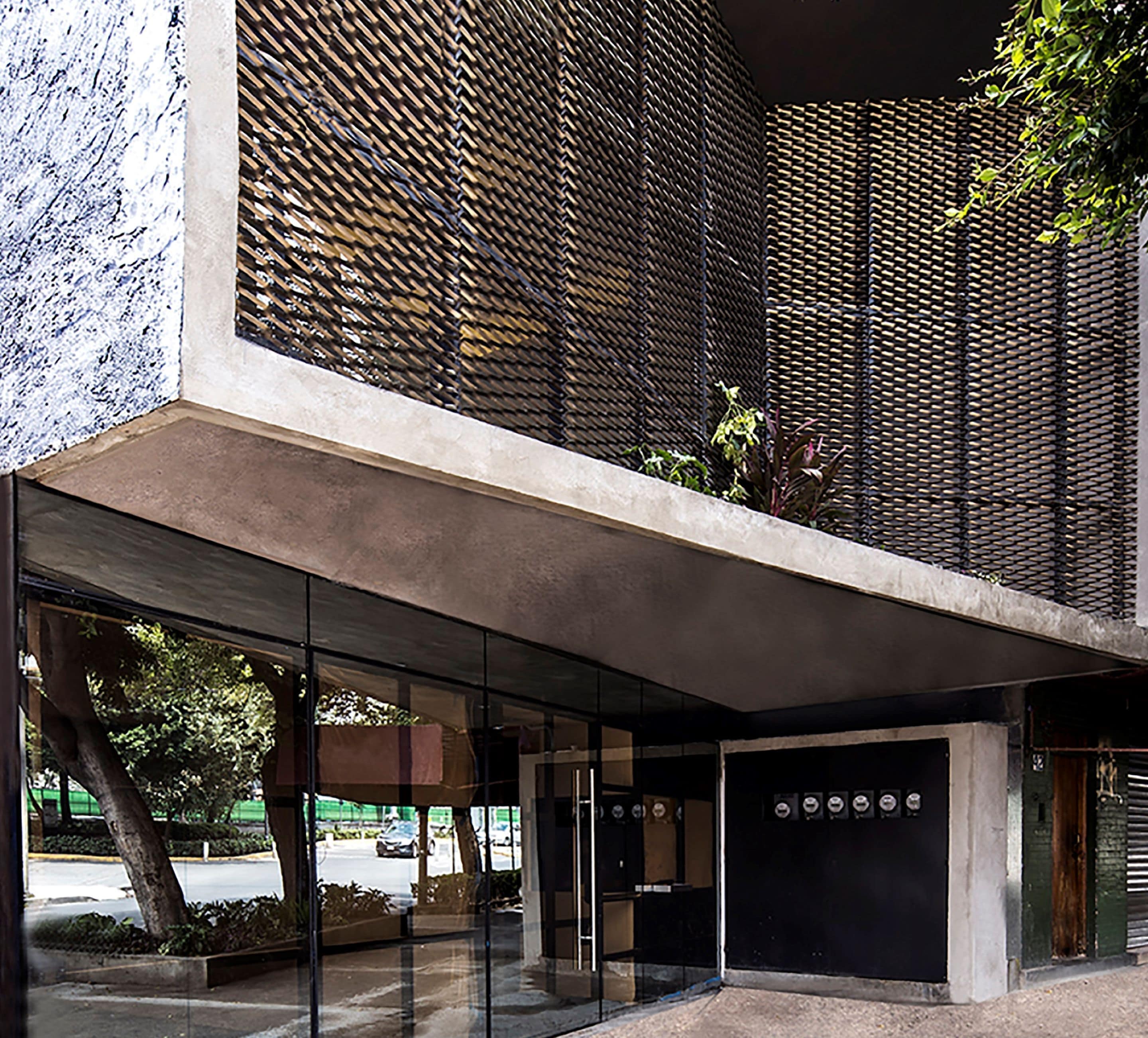 A modern building with a concrete facade, large glass windows, and a metal mesh pattern.