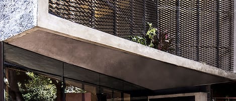 A modern building with a concrete facade, large glass windows, and a metal mesh pattern.