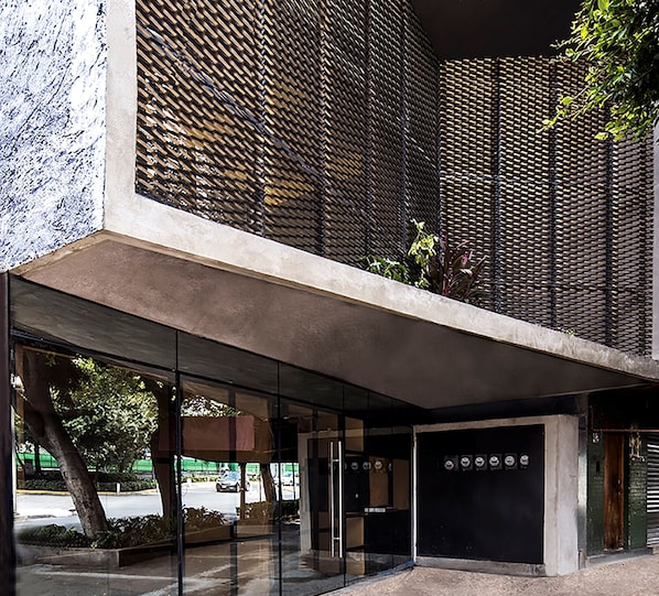 A modern building with a concrete facade, large glass windows, and a metal mesh pattern.