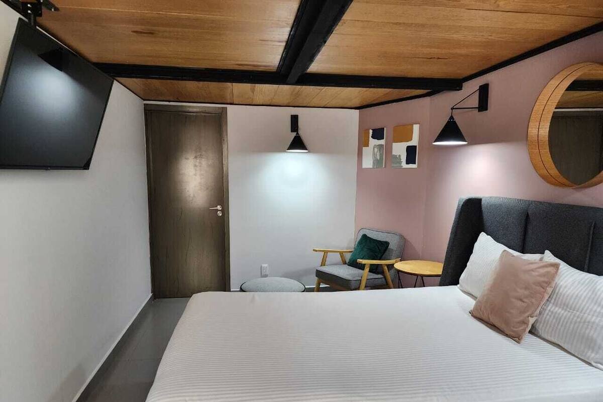 Un dormitorio con una cama, una silla, una mesita, un espejo redondo y una puerta.