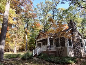 A rustic cabin with a stone chimney, surrounded by autumn foliage. - Relaxing Woodsy Cottage Retreat: Perfect for Families & Friends [Sleeps 8] (Michigan City)