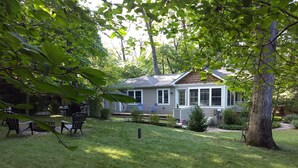 A house with a covered patio, a lawn, and a fire pit area. - Relaxing Woodsy Cottage Retreat: Perfect for Families & Friends [Sleeps 8] (Michigan City)