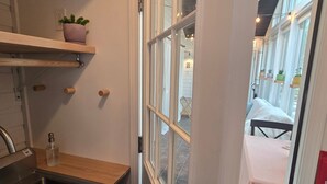 A kitchen with a sink, wooden shelves, a potted plant, and a window with a view of a dining area. - Relaxing Woodsy Cottage Retreat: Perfect for Families & Friends [Sleeps 8] (Michigan City)