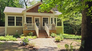 A two-story house with a front porch, a stone pathway leading to the entrance, and a garden with various plants. - Relaxing Woodsy Cottage Retreat: Perfect for Families & Friends [Sleeps 8] (Michigan City)