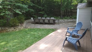 A wooden deck with a stone wall, a grassy lawn, and a dining area with chairs and a table. - Relaxing Woodsy Cottage Retreat: Perfect for Families & Friends [Sleeps 8] (Michigan City)