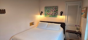 A bedroom with a bed, a painting, wall sconces, a door, and a small table with a plant. - Relaxing Woodsy Cottage Retreat: Perfect for Families & Friends [Sleeps 8] (Michigan City)