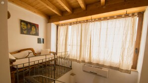 Ein Zimmer mit einer Holztreppe, einem Bett mit Kopfteil, einem Fenster mit Vorhängen und einer Wand-Klimaanlage.