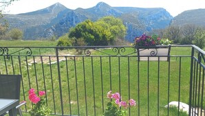 A balcony with a metal railing, a table, and chairs. In the background, there is a grassy area with trees and mountains. - Charming gîte 300m from the picturesque village of Rougon (Rougon)