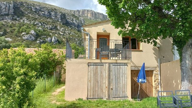 A two-story building with a balcony, a wooden gate, and a blue umbrella. - Charming gîte 300m from the picturesque village of Rougon (Rougon)