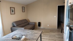 A living room with a grey sofa, a coffee table, and a kitchen area with a fridge and oven. - Charming gîte 300m from the picturesque village of Rougon (Rougon)