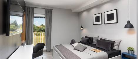 Un dormitorio moderno con cama, mesitas de noche, un escritorio y un ventanal con cortinas.