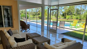 A covered outdoor seating area with wicker furniture, a pool, and a view of a landscaped garden.