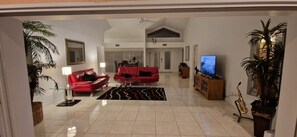 Uma sala de estar ampla com um sofá vermelho, uma televisão, um saxofone e uma planta em vaso.