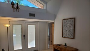 A room with a door, a floor lamp, a wooden console table, and a framed artwork on the wall.