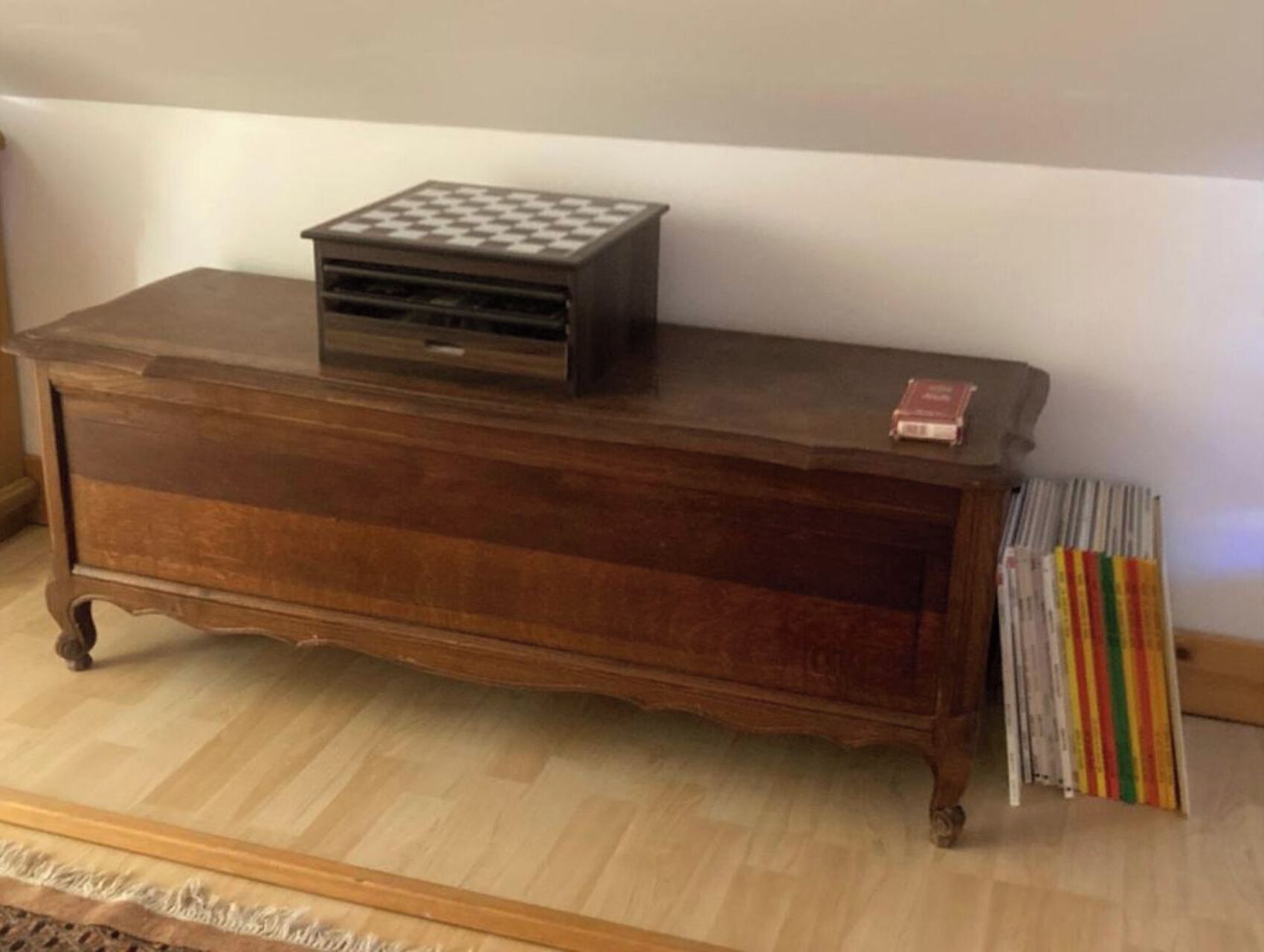 A wooden dresser with drawers and a top cabinet, a small black object on top, and a striped fabric hanging on the right.