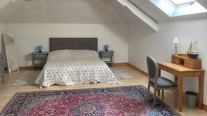 Um quarto com teto inclinado, um claraboia, uma cama com colcha estampada, uma escrivaninha com cadeira e um tapete grande.