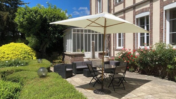 Um pátio externo com mesa e cadeiras, um grande guarda-sol e um solário.