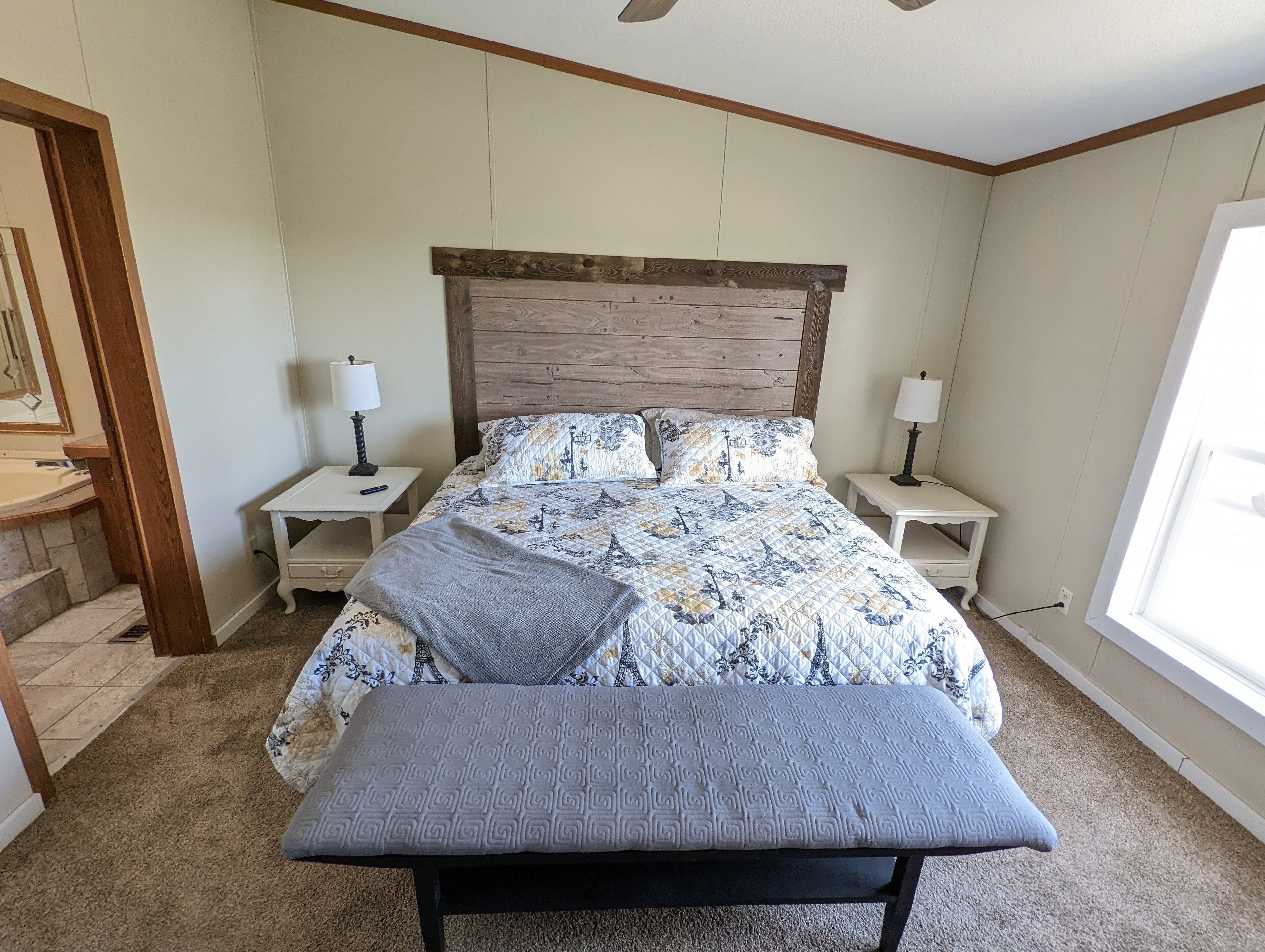 A bedroom with a bed, two bedside tables, a bench, a window, and a door.