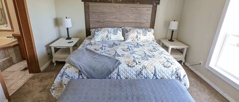 A bedroom with a bed, two bedside tables, a bench, a window, and a door.