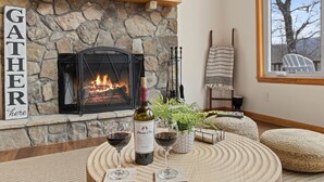 Una chimenea de piedra con fuego, una botella de vino y copas sobre una mesa de fibras naturales.