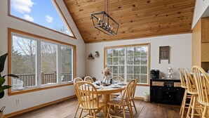Un comedor con mesa y sillas de madera, ventanas amplias y techo con vigas de madera.